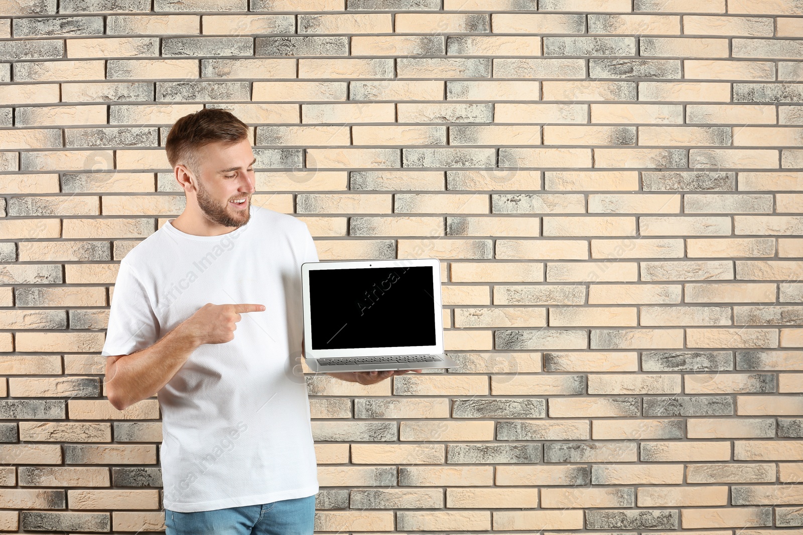 Photo of Young handsome man with laptop on brick wall background