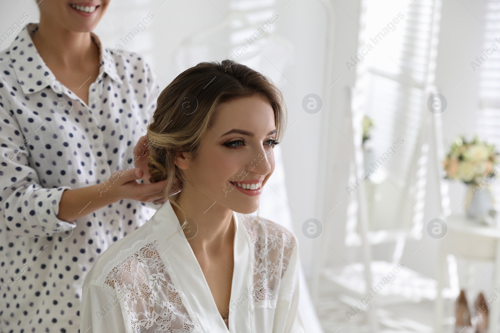 Photo of Professional stylist making wedding hairstyle for bride in salon