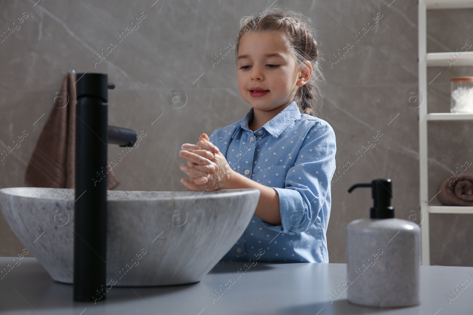 Photo of Cute little girl washing hands with liquid soap in bathroom