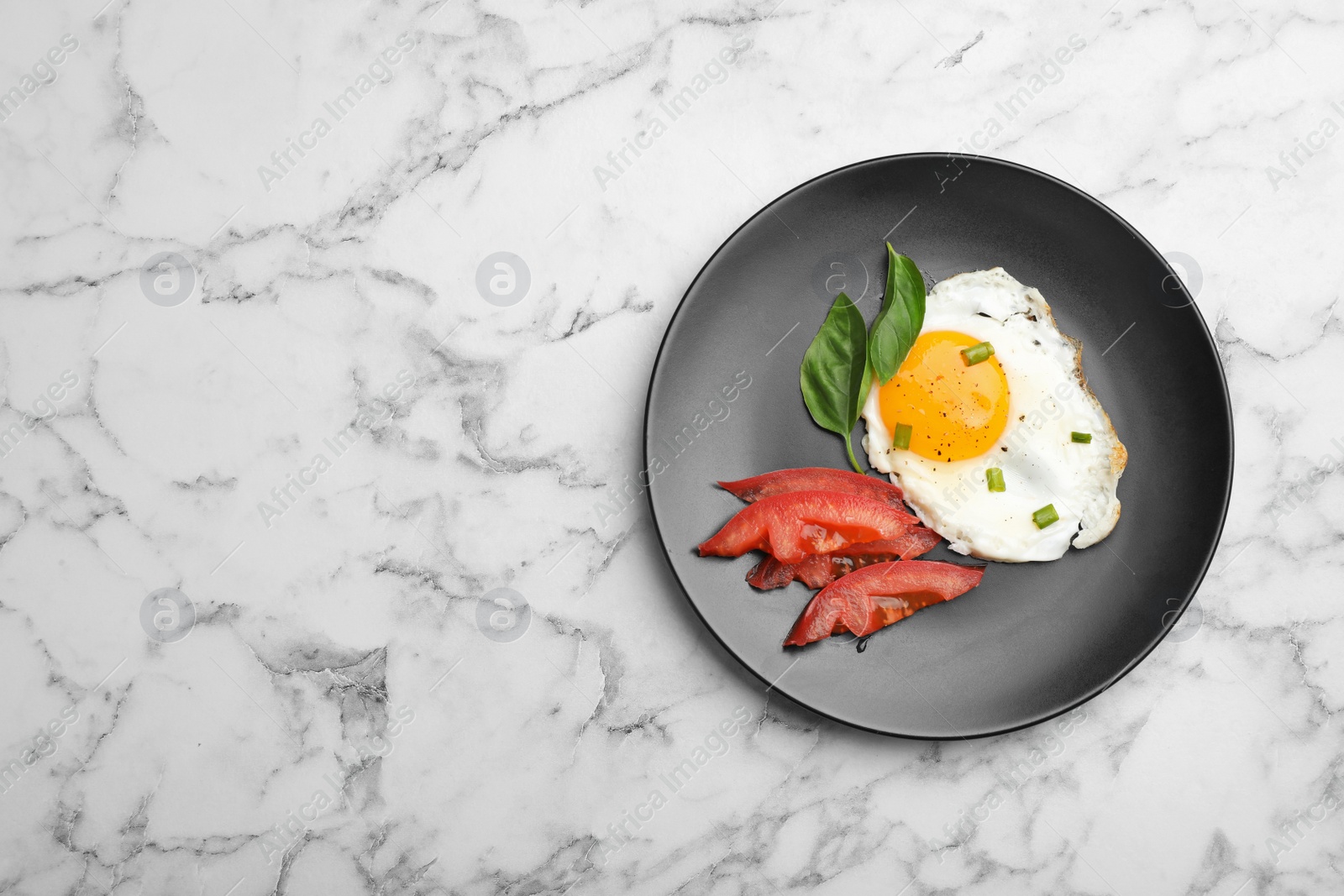 Photo of Plate with fried sunny side up egg and tomato on marble background, top view. Space for text