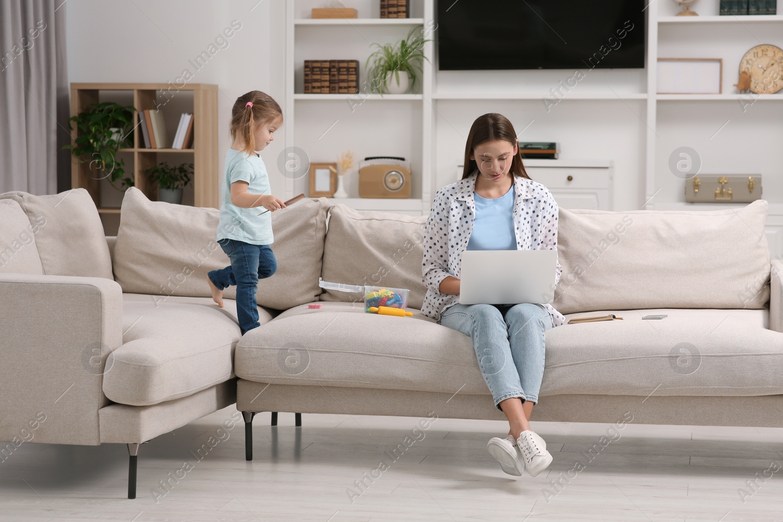 Photo of Little daughter playing while her mother working remotely on sofa at home