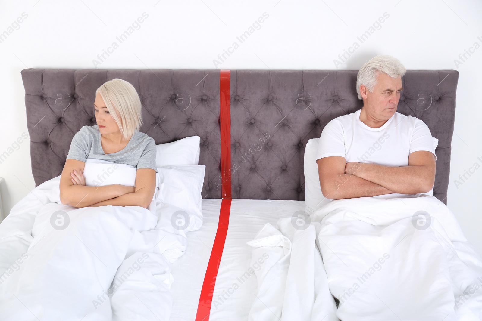 Photo of Upset mature couple with relationship problems lying separately in bed at home