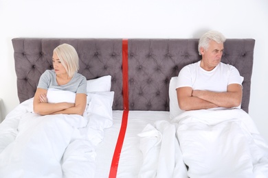 Upset mature couple with relationship problems lying separately in bed at home