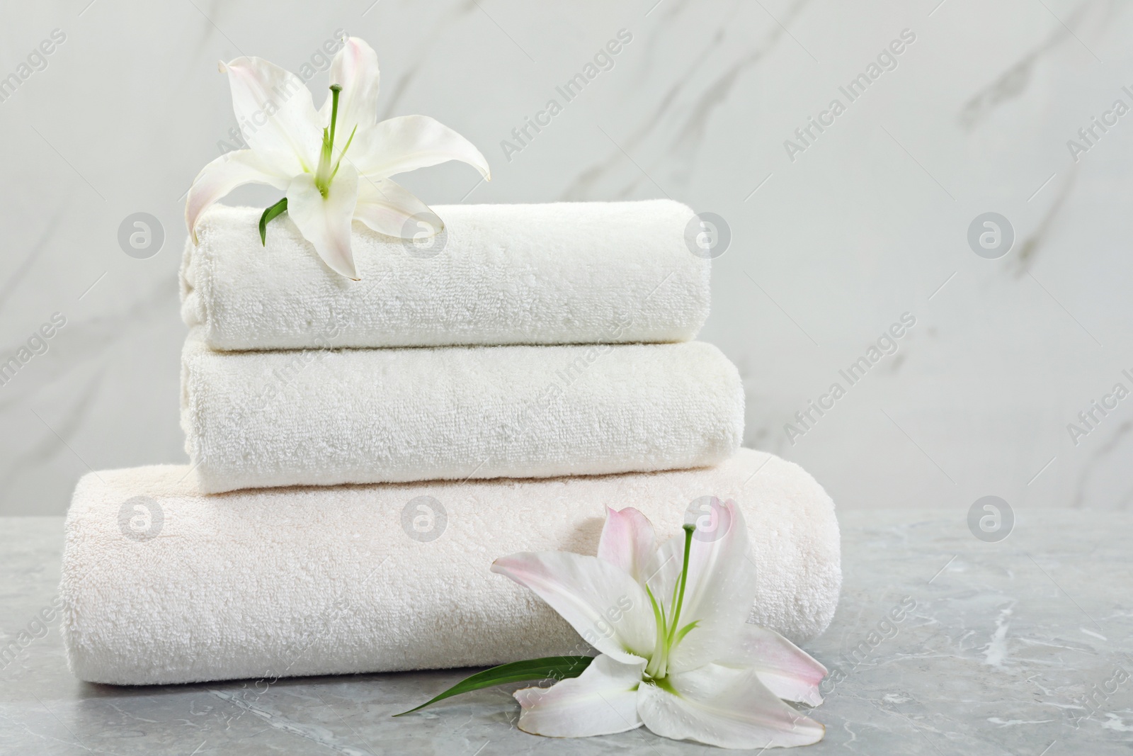 Photo of Stack of fresh towels with flowers on grey table against light background. Space for text