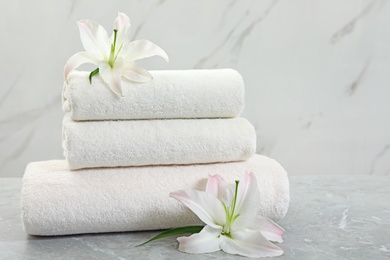 Stack of fresh towels with flowers on grey table against light background. Space for text