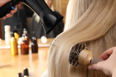 Photo of Hairdresser blow drying client's hair in salon, closeup