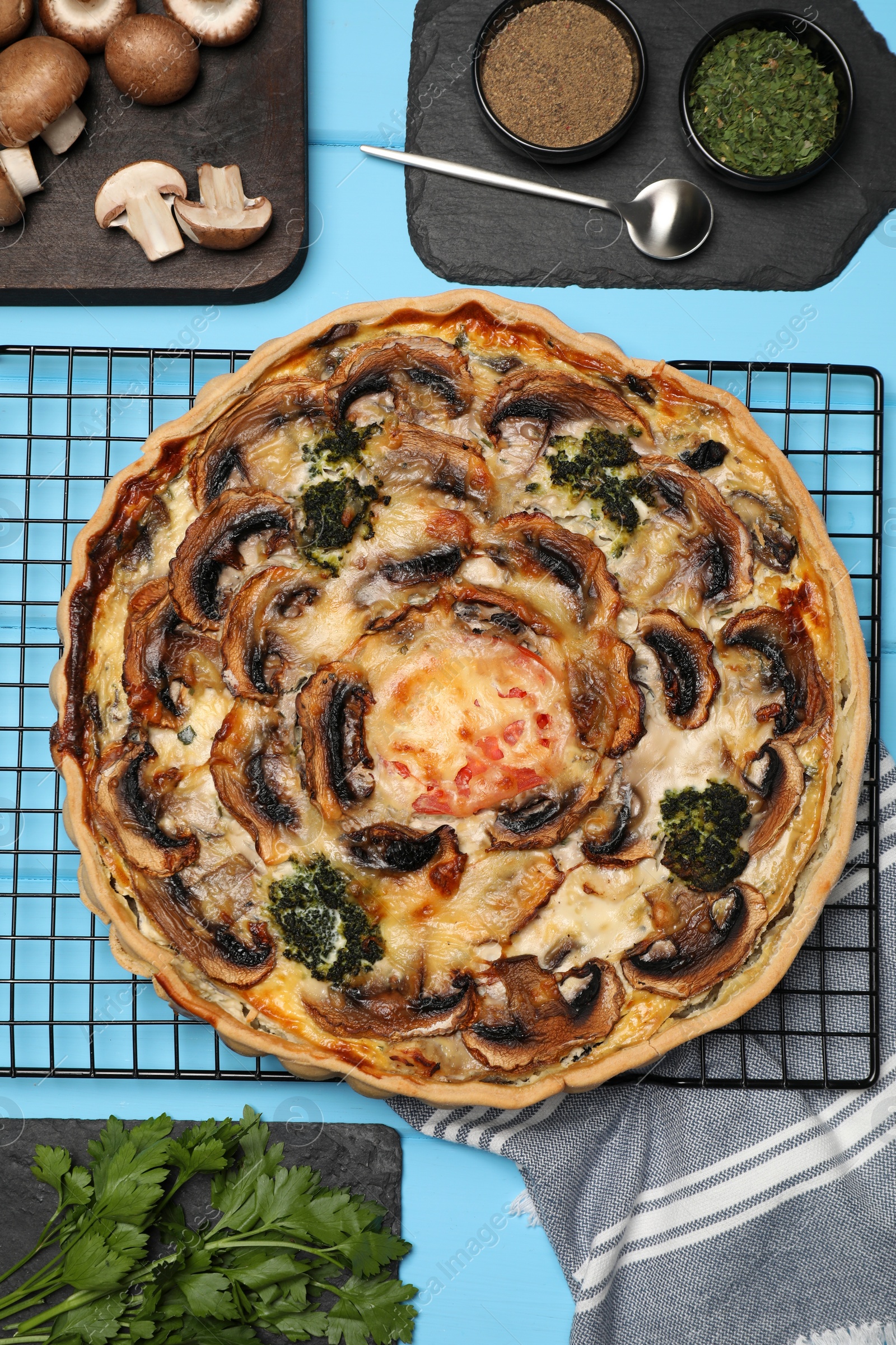 Photo of Delicious quiche with mushrooms and ingredients on light blue wooden table, flat lay