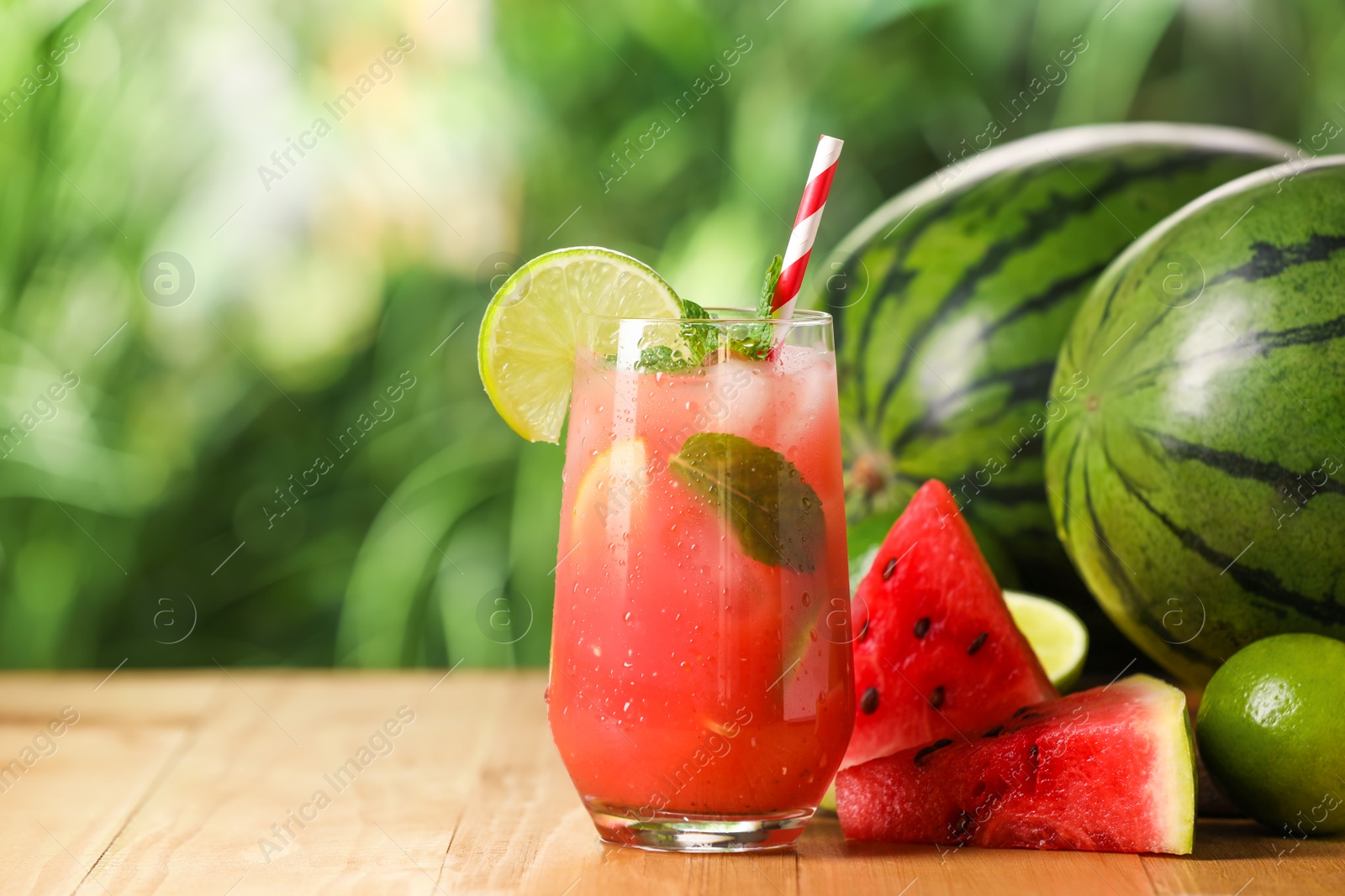 Photo of Glass of freshly made watermelon juice with lime and mint on wooden table outdoors