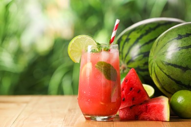 Photo of Glass of freshly made watermelon juice with lime and mint on wooden table outdoors