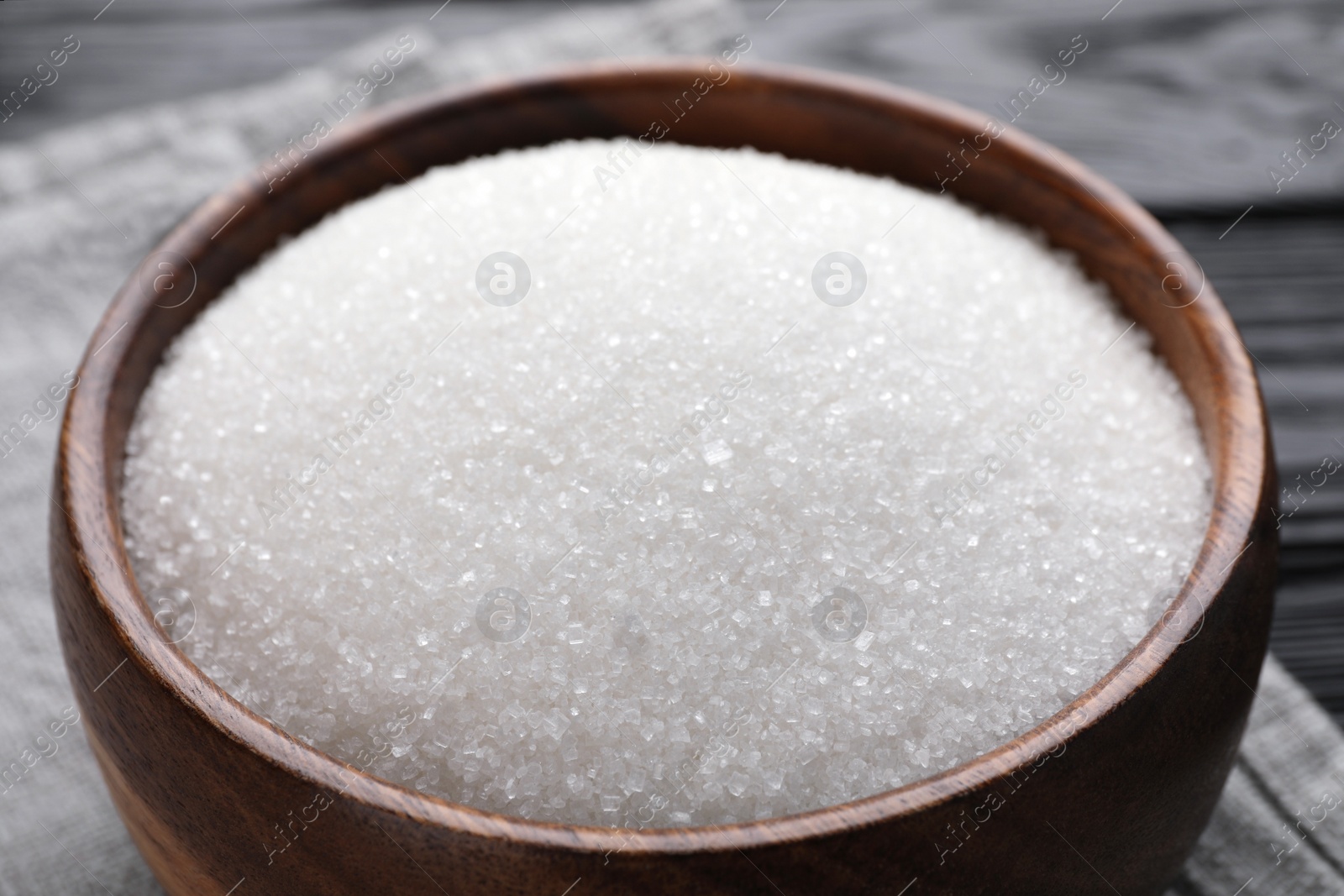 Photo of Granulated sugar in wooden bowl on table, closeup