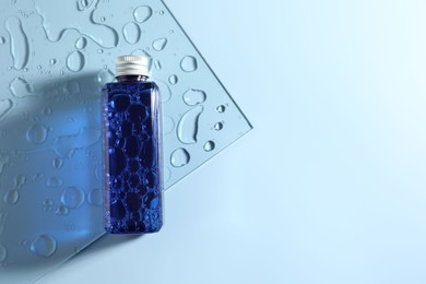 Bottle of cosmetic product on light blue background, top view. Space for text