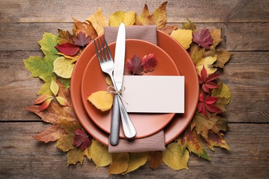 Photo of Festive table setting with autumn leaves and blank card on wooden background, flat lay