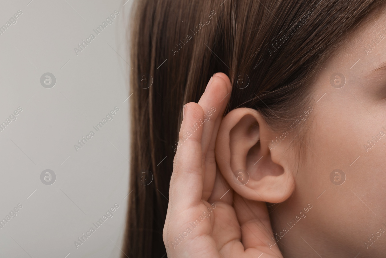 Photo of Little girl with hearing problem on grey background, closeup. Space for text