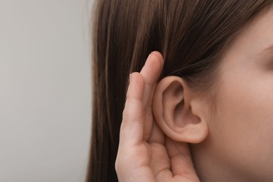 Photo of Little girl with hearing problem on grey background, closeup. Space for text