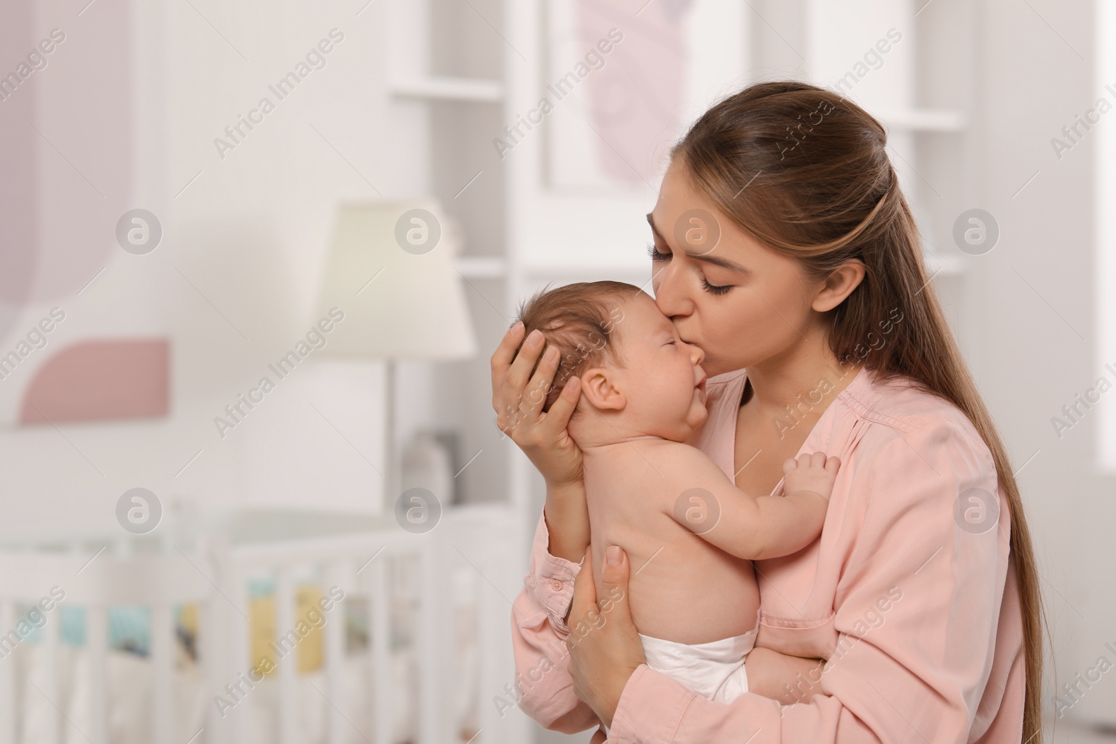 Photo of Mother kissing her cute newborn baby in child's room, space for text