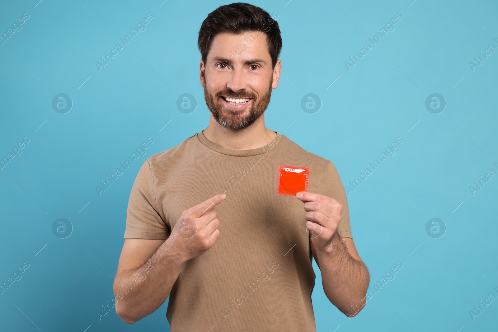 Photo of Happy man holding condom on light blue background. Safe sex