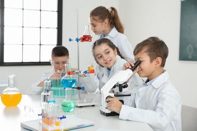 Photo of Schoolboy looking through microscope and his classmates at chemistry lesson
