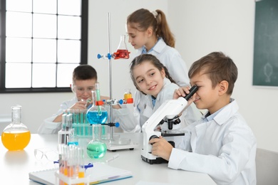 Schoolboy looking through microscope and his classmates at chemistry lesson