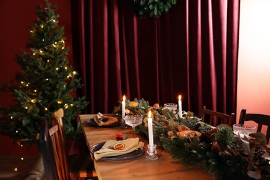 Dining table with burning candles and Christmas decor in stylish room. Interior design