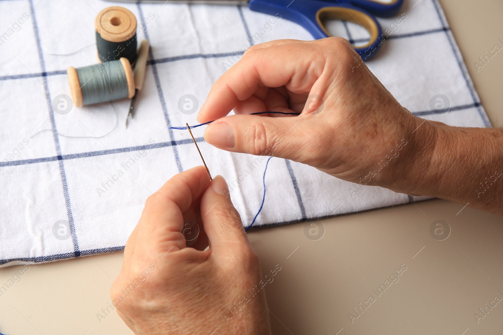 Photo of Closeup view of woman threading needle at beige table