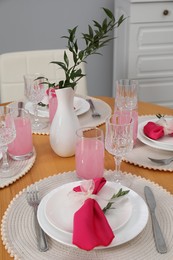 Photo of Color accent table setting. Glasses, plates, vase with green branch and pink napkins in dining room