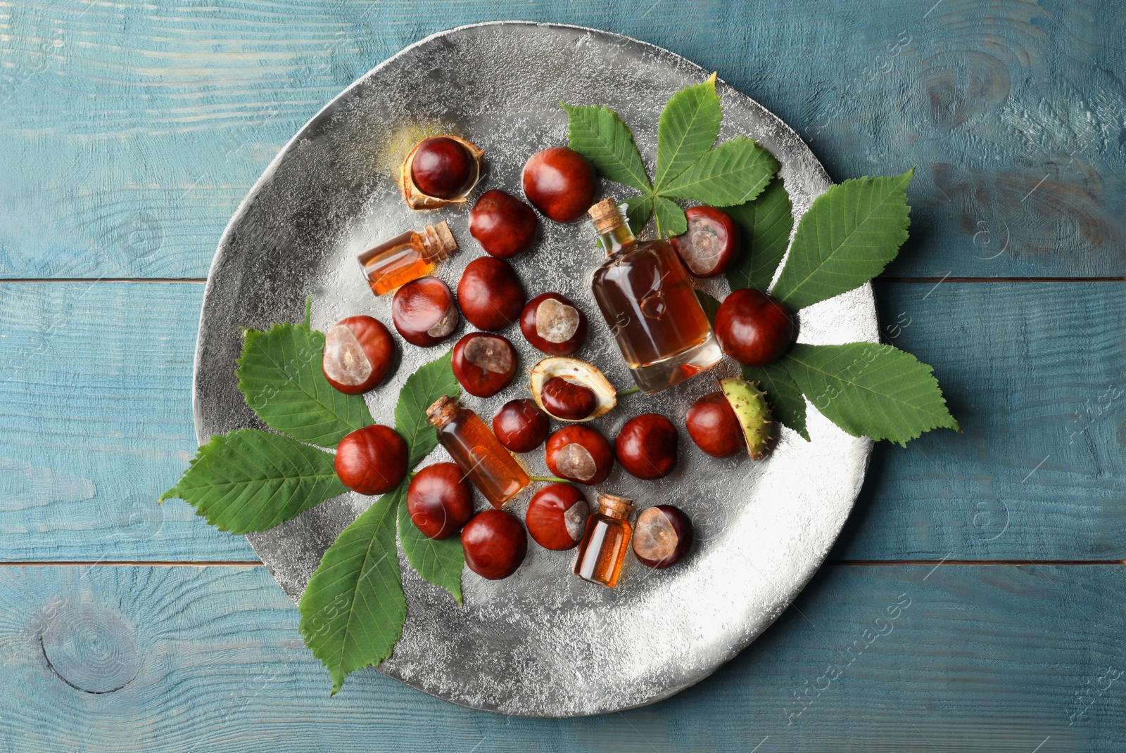 Photo of Chestnuts, leaves and bottles of essential oil on blue wooden table, top view