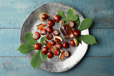 Chestnuts, leaves and bottles of essential oil on blue wooden table, top view