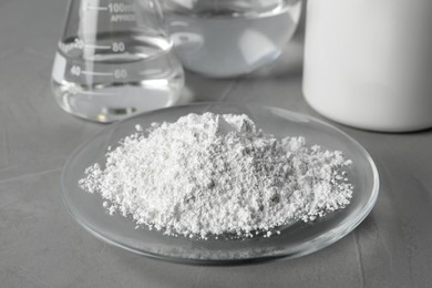 Photo of Plate with calcium carbonate powder and laboratory glassware on grey table, closeup