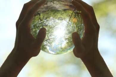 Photo of Green trees outdoors, overturned reflection. Man holding crystal ball in forest, closeup