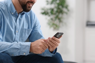 Young man using smartphone in office, closeup. Space for text