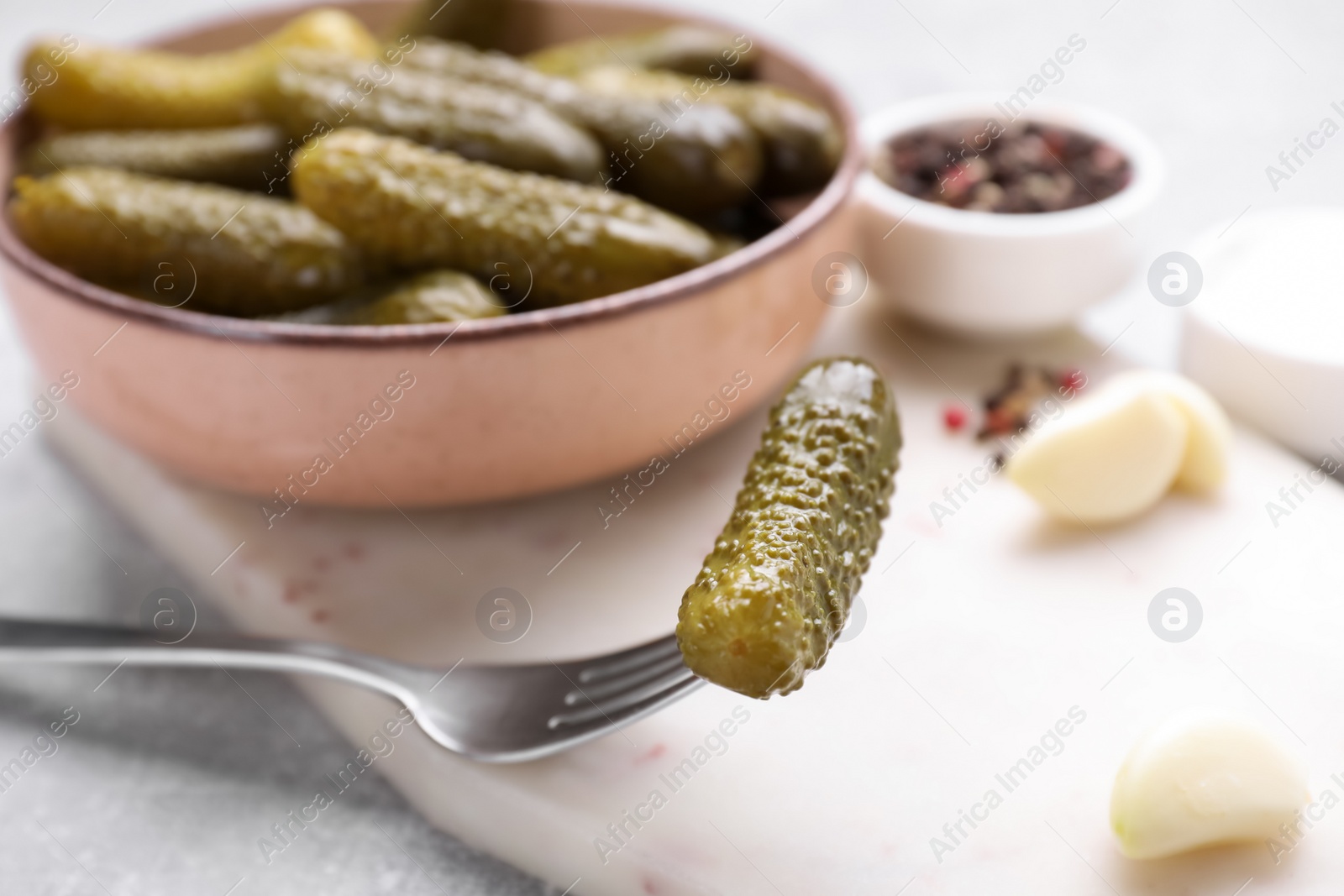 Photo of Fork and bowl with pickled cucumber on light table, closeup