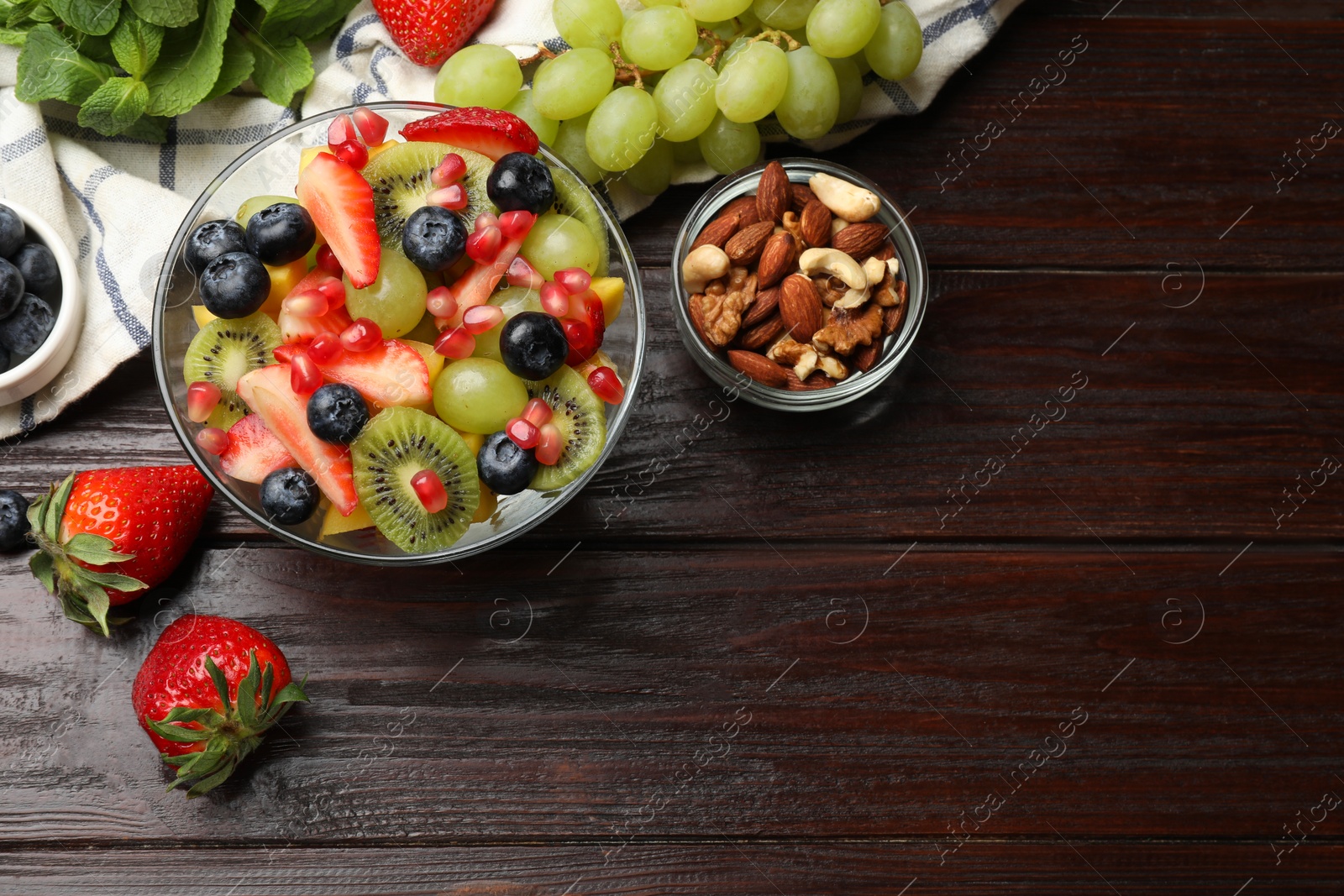 Photo of Tasty fruit salad in bowl and ingredients on wooden table, flat lay. Space for text