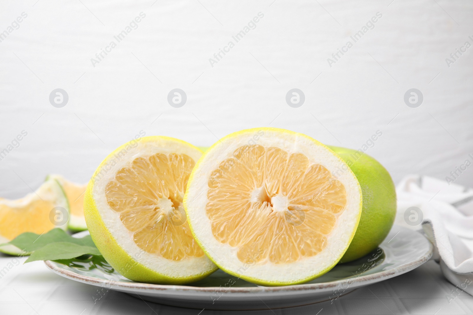 Photo of Whole and cut sweetie fruits with green leaves on white tiled table