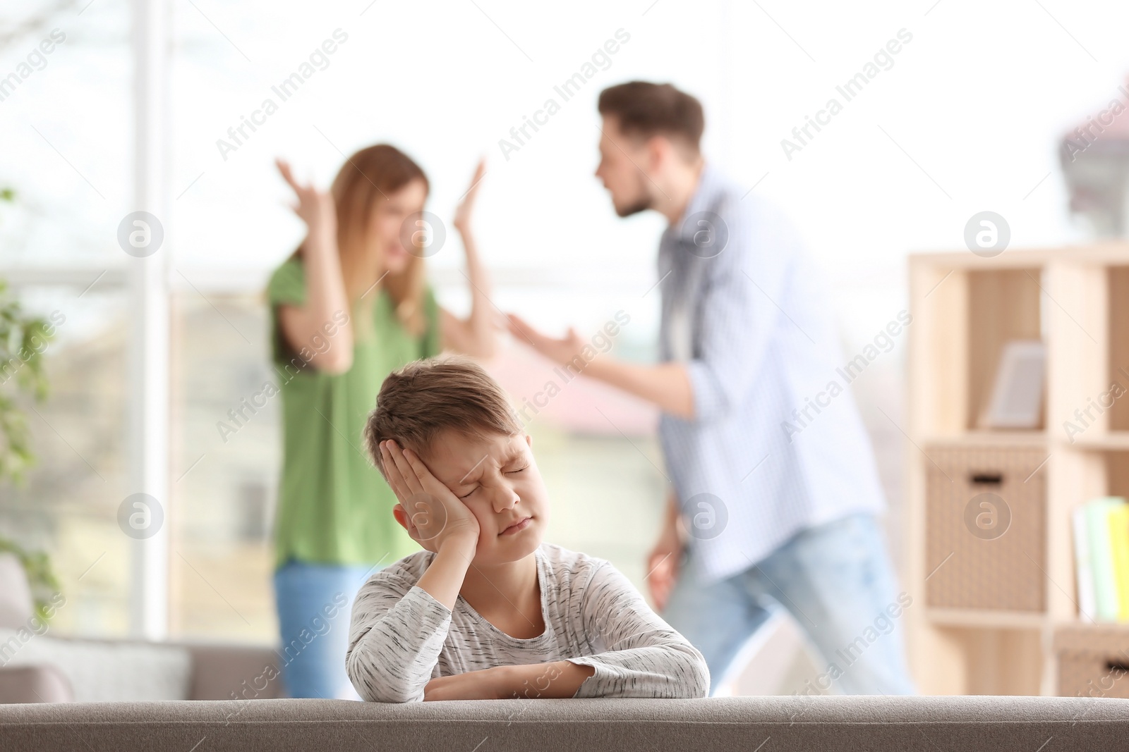 Photo of Little unhappy boy sitting on sofa while parents arguing at home