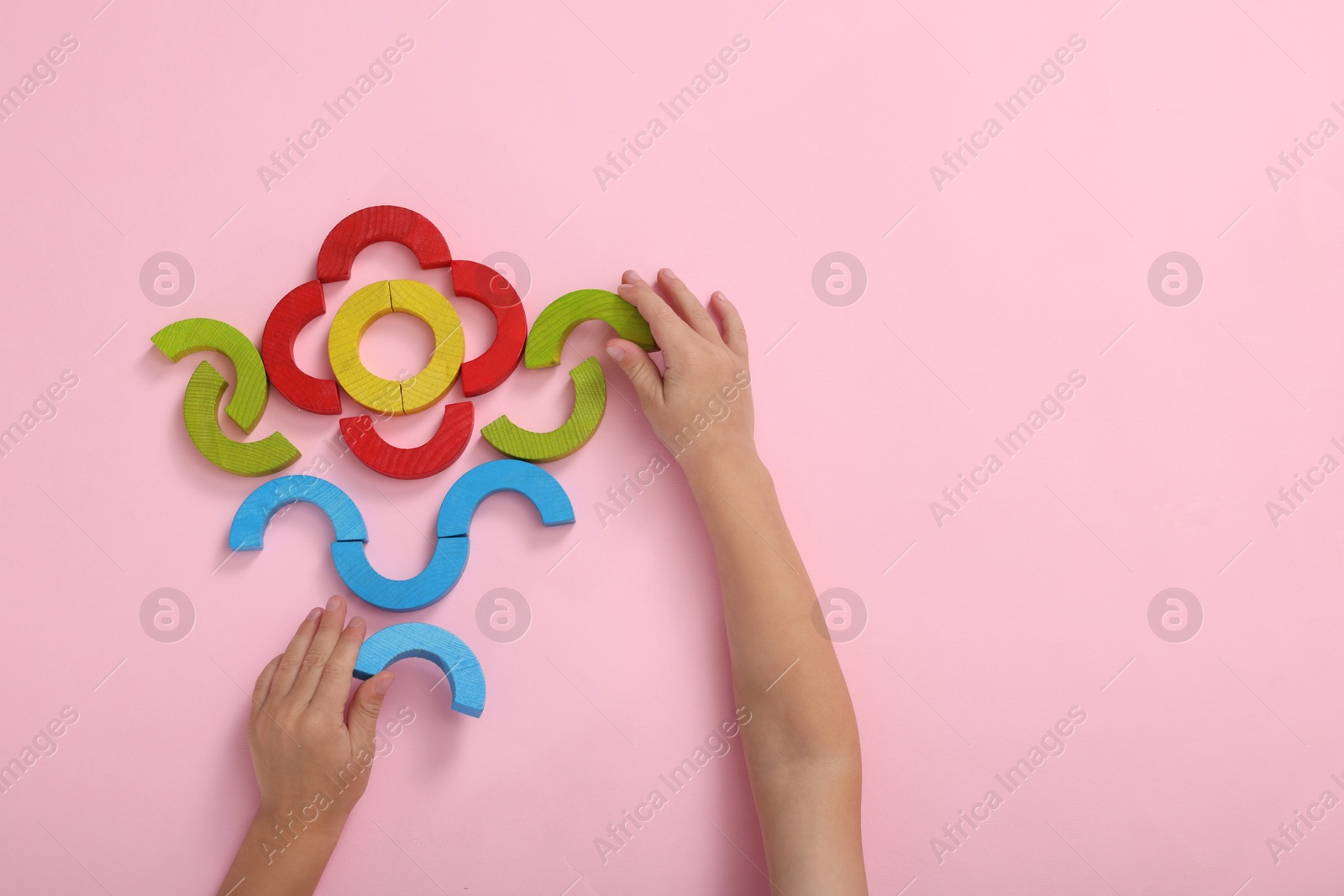 Photo of Motor skills development. Boy playing with colorful wooden arcs at pink table, top view. Space for text