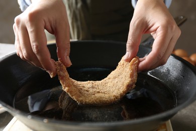 Photo of Cooking schnitzel. Woman putting raw pork chop in bread crumbs into frying pan, closeup