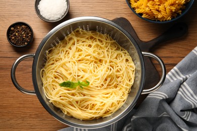 Cooked pasta in metal colander and spices on wooden table, flat lay