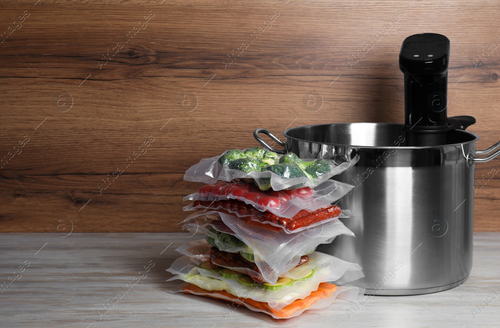 Photo of Sous vide cooking. Thermal immersion circulator in pot and vacuum packed food products on white wooden table. Space for text