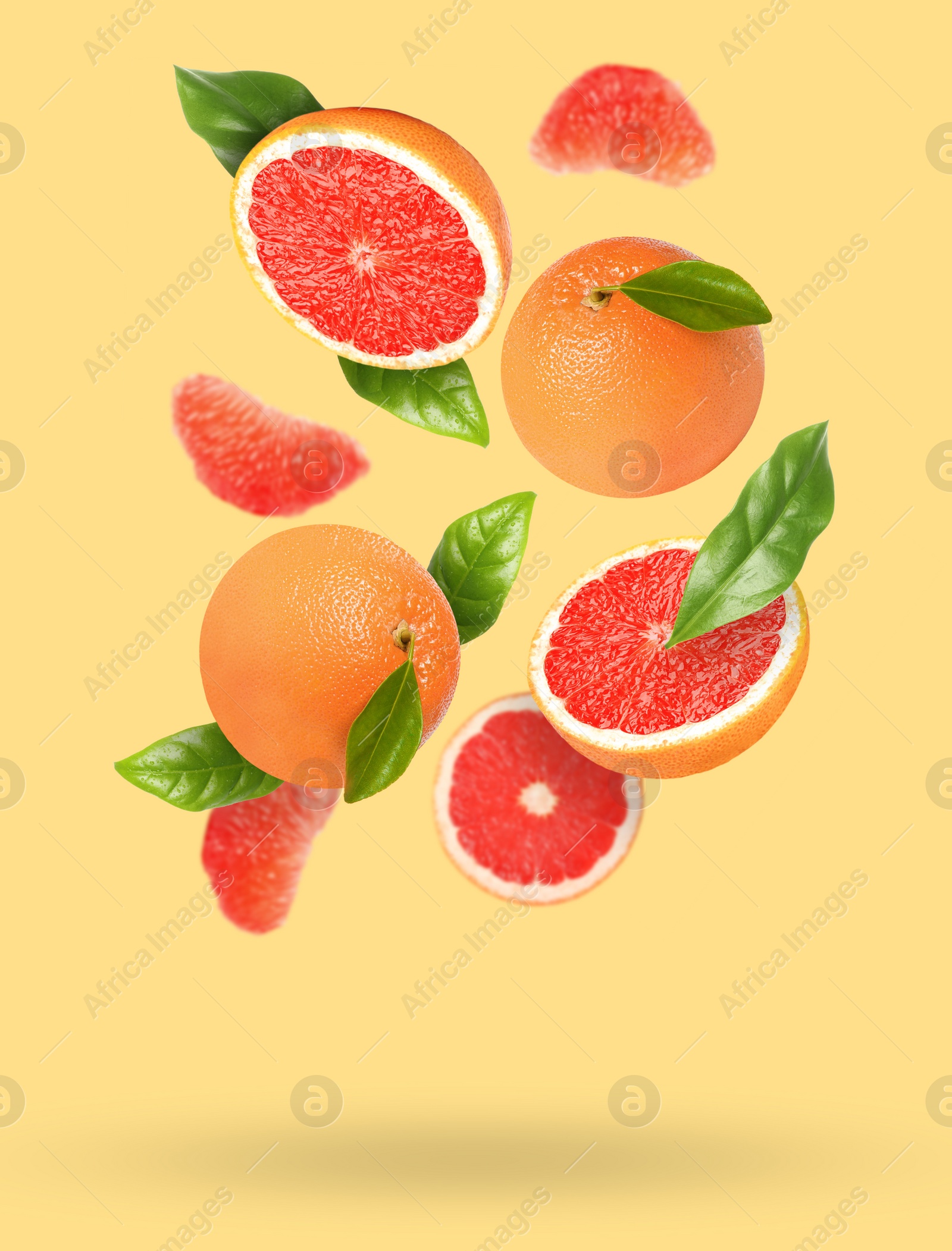 Image of Tasty ripe grapefruits and green leaves falling on beige background