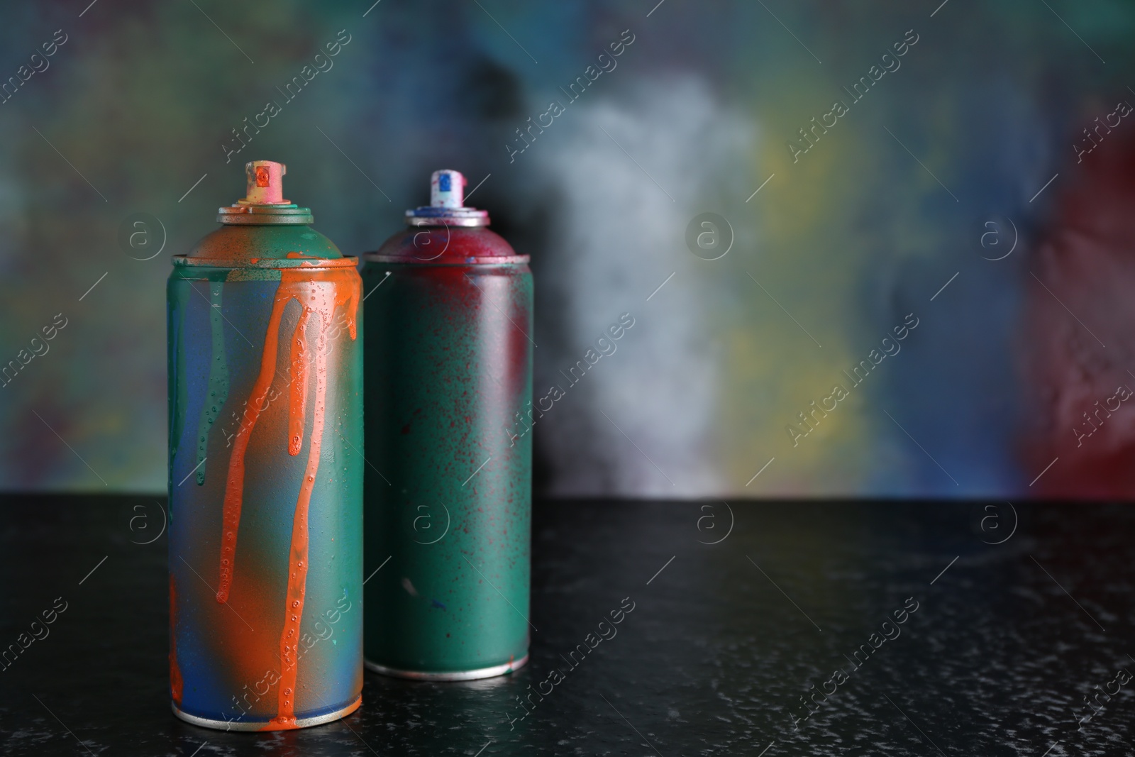 Photo of Two spray paint cans on black textured surface against color background, space for text