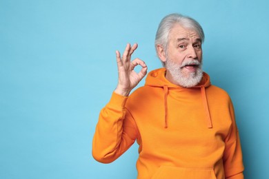 Senior man with mustache showing ok gesture on light blue background, space for text