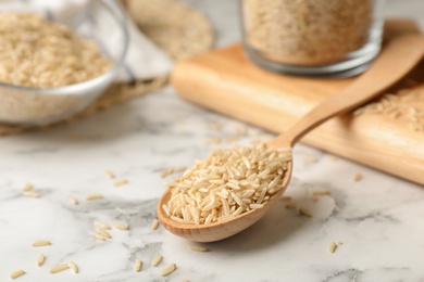 Photo of Uncooked brown rice in wooden spoon on table. Space for text