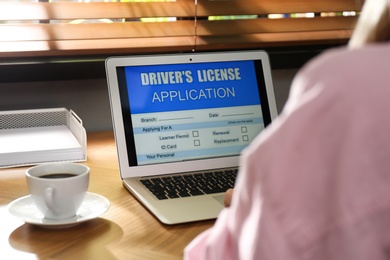 Woman using laptop to fill driver's license application form at table in office, closeup