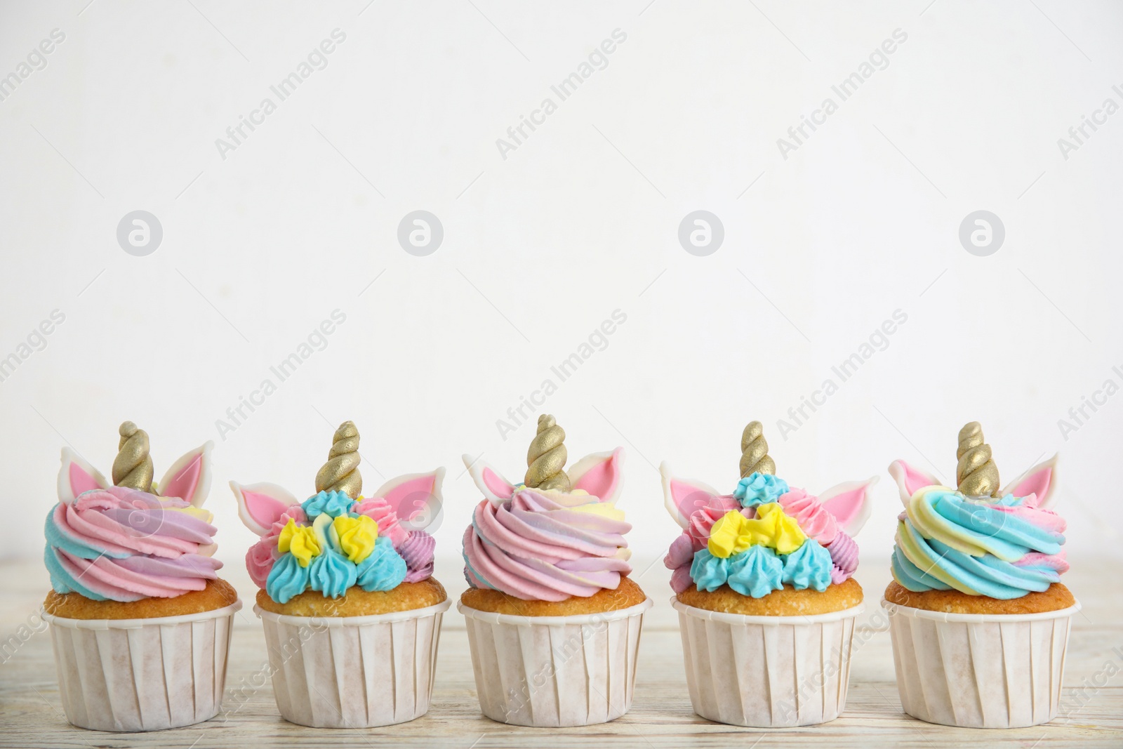 Photo of Many cute sweet unicorn cupcakes on white wooden table