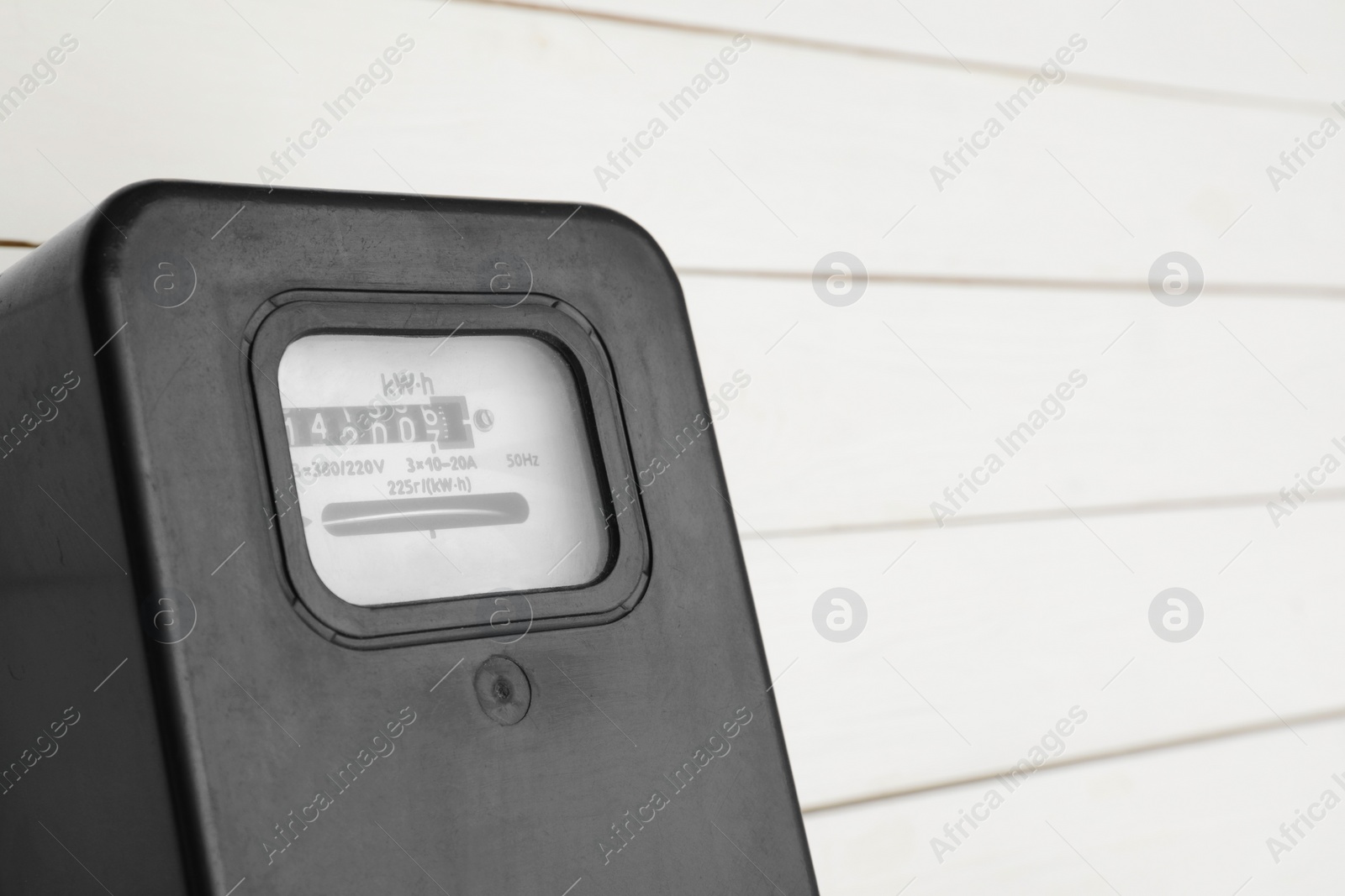 Photo of Black electric meter on white wooden wall, closeup with space for text. Measuring device