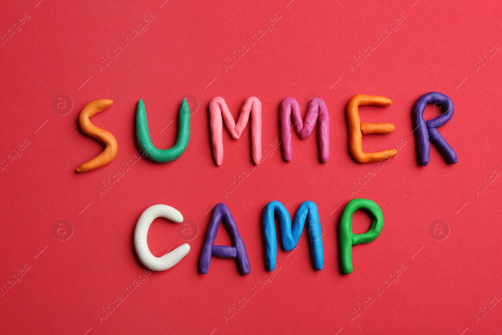 Photo of Phrase SUMMER CAMP made of colorful clay on red background, flat lay