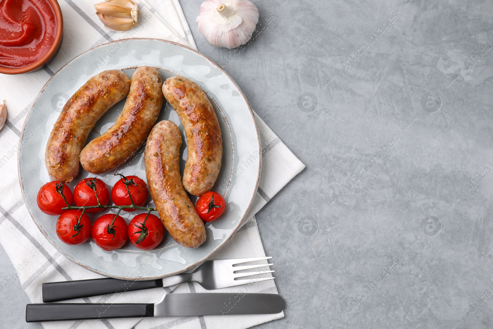 Photo of Tasty homemade sausages, tomatoes, garlic and ketchup on grey textured table, flat lay. Space for text