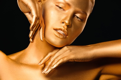 Photo of Portrait of beautiful lady with gold paint on skin against black background, closeup