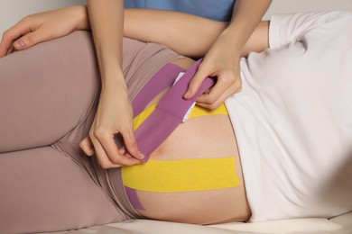 Photo of Pregnant woman visiting physiotherapist. Doctor applying kinesio tape on couch, closeup