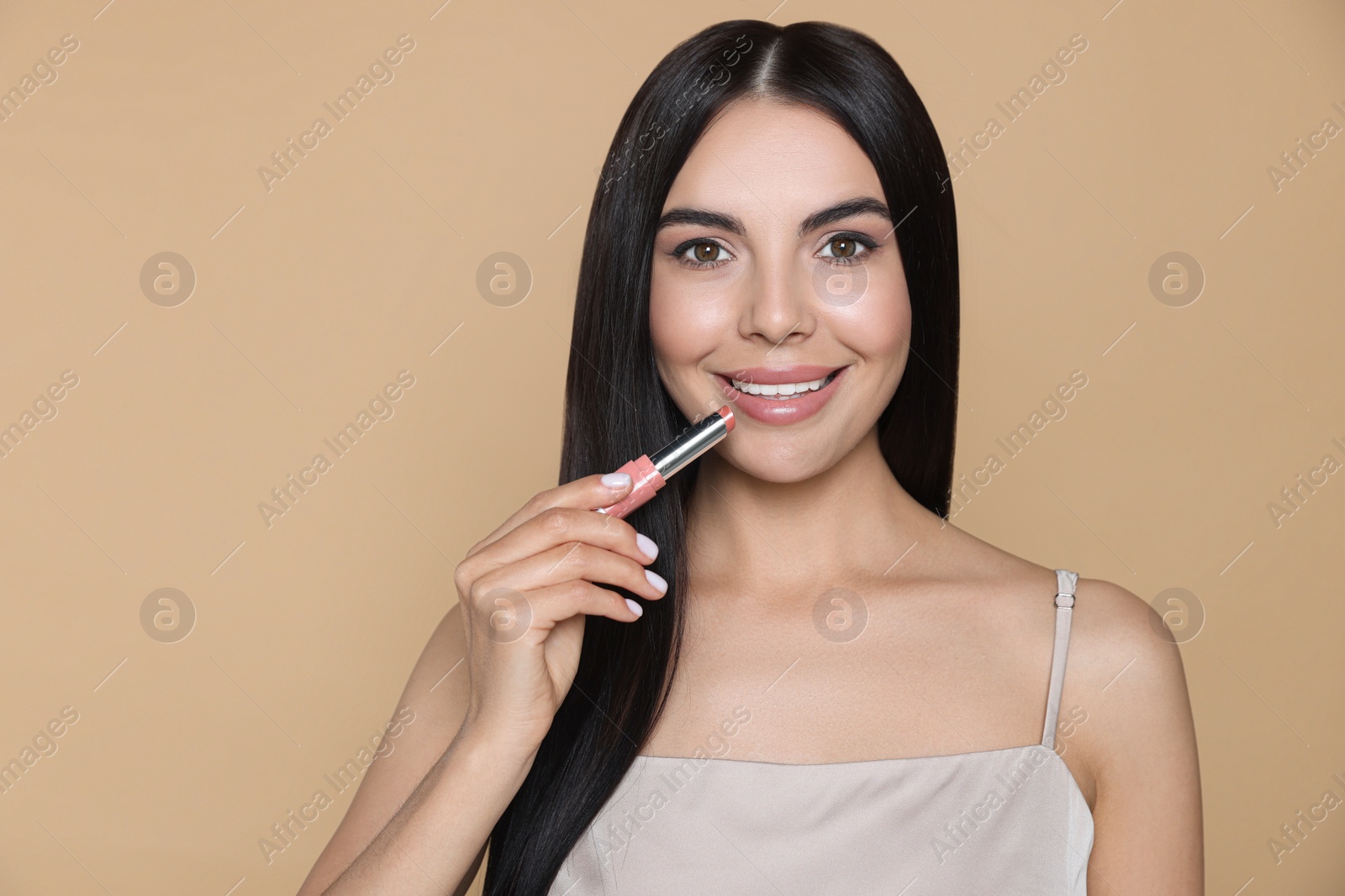 Photo of Young woman with beautiful makeup holding nude lipstick on beige background